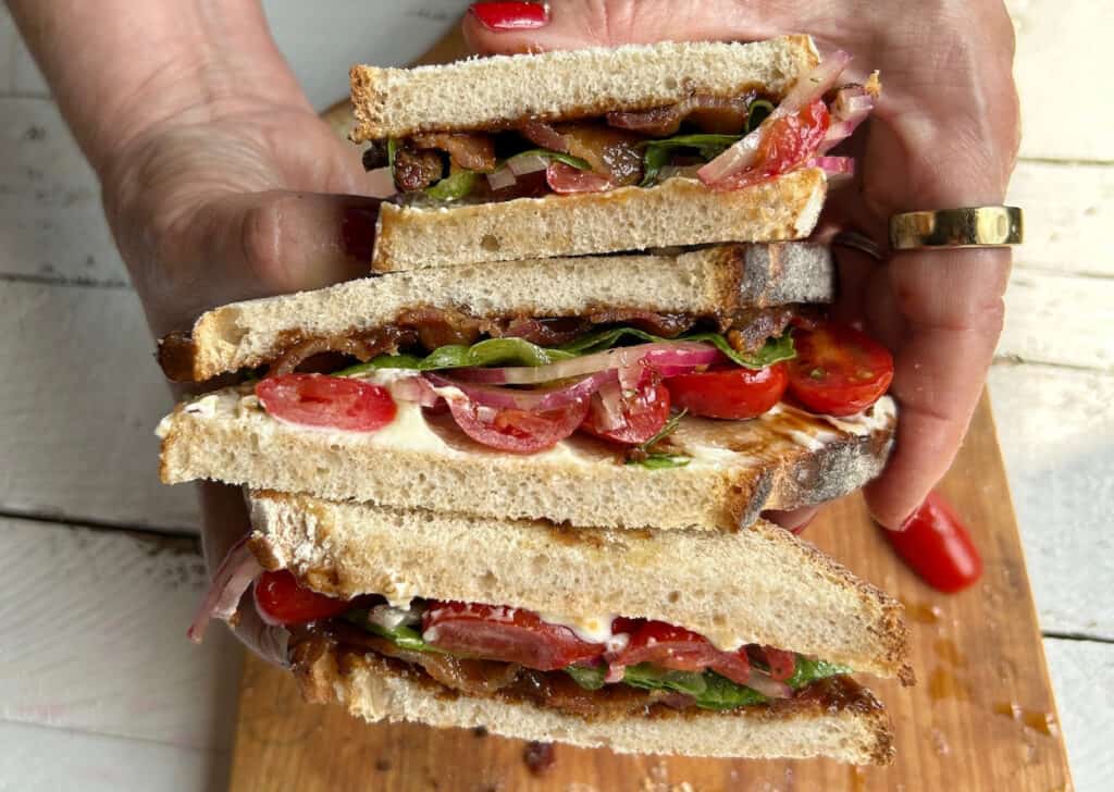 two hands holding No Crumbs Left's BLT with Chipotle Prune Jam