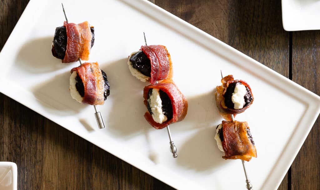 a white plate of Devils on Horseback with Goat Cheese skewered with a toothpick