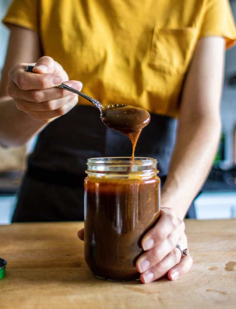 woman pulling a spoon covered in prune purée out of a jar