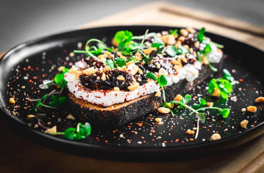 Five Spice California Prune Jam on top a a piece of toast with ricotta and microgreens