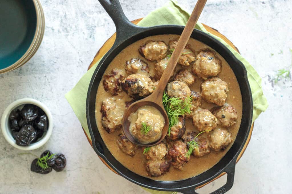a cast iron pan filled with swedish meatballs and a bowl of prunes