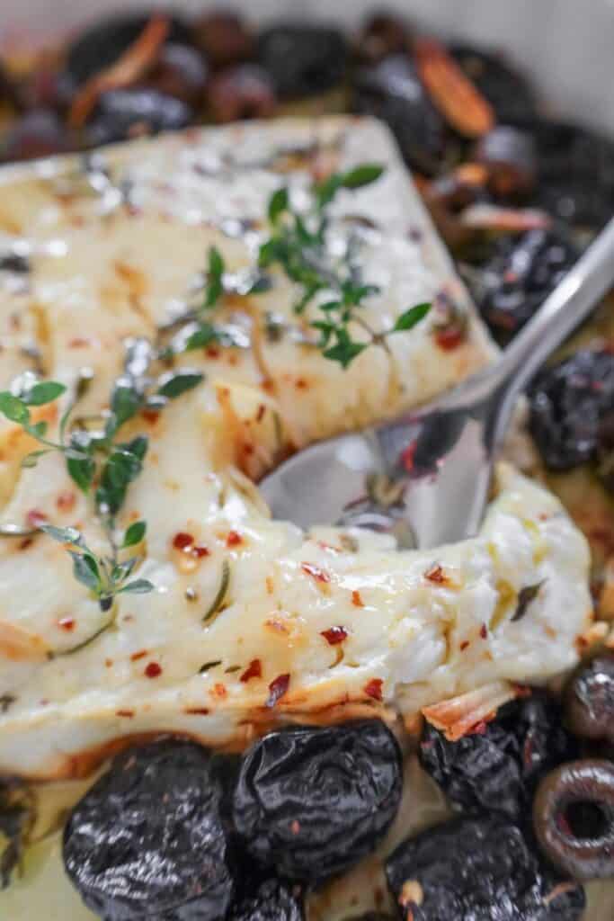scooping a spoonful of baked feta that is surrounded by prunes and olives