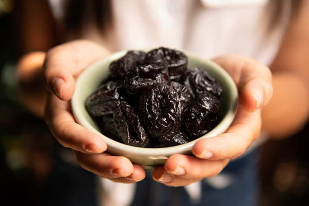 two hands holding a small bowl of prunes