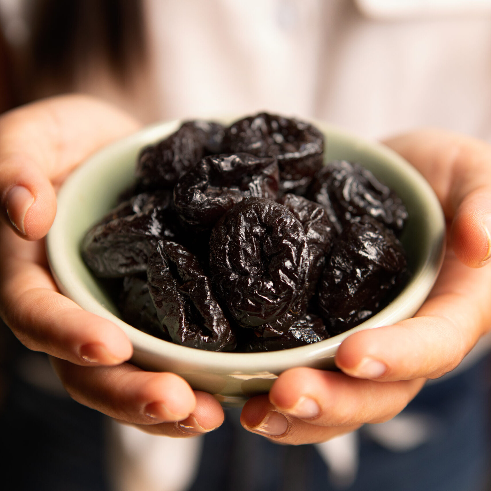 prunes may preserve bone health - two hands holding a small bowl of prunes
