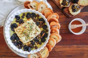 horizontal image of baked feta in a white dish with california prunes and olives