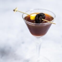 prune manhattan in a chilled glass with a syrupy prune garnish