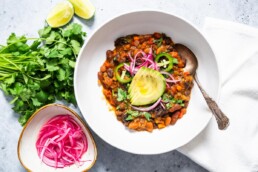 horizontal image of vegan chili garnished with avocado and pickled onions