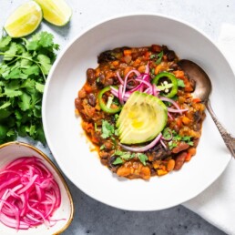 horizontal image of vegan chili garnished with avocado and pickled onions