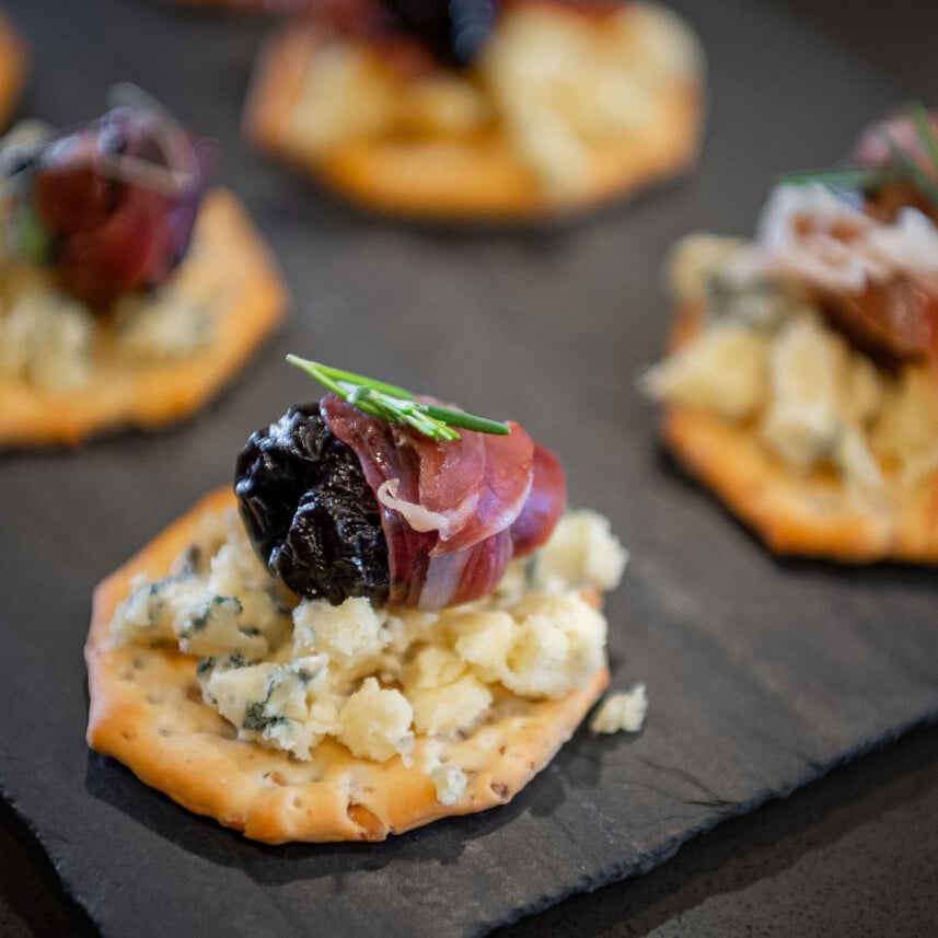 proscuitto wrapped prune blue cheese appetizer on a cracker on a black tray