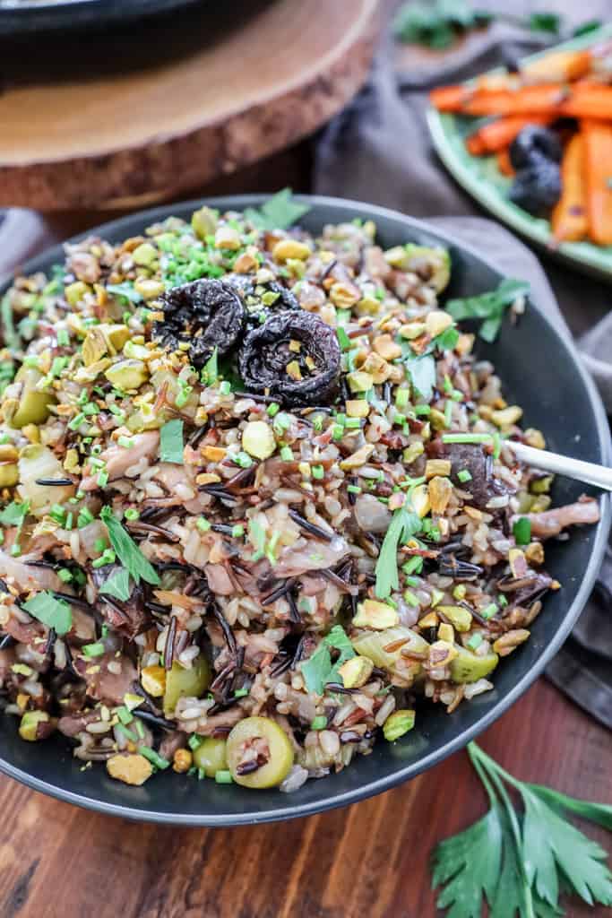 wild rice pilaf in a black serving bowl topped with prunes