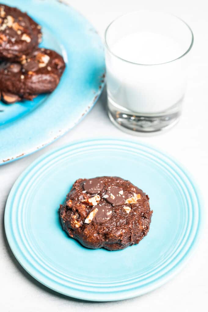 a chocolate pecan cookie on a plate with a glass of milk