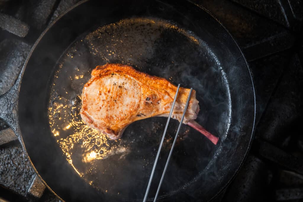 searing pork chops in a black cast iron skillet