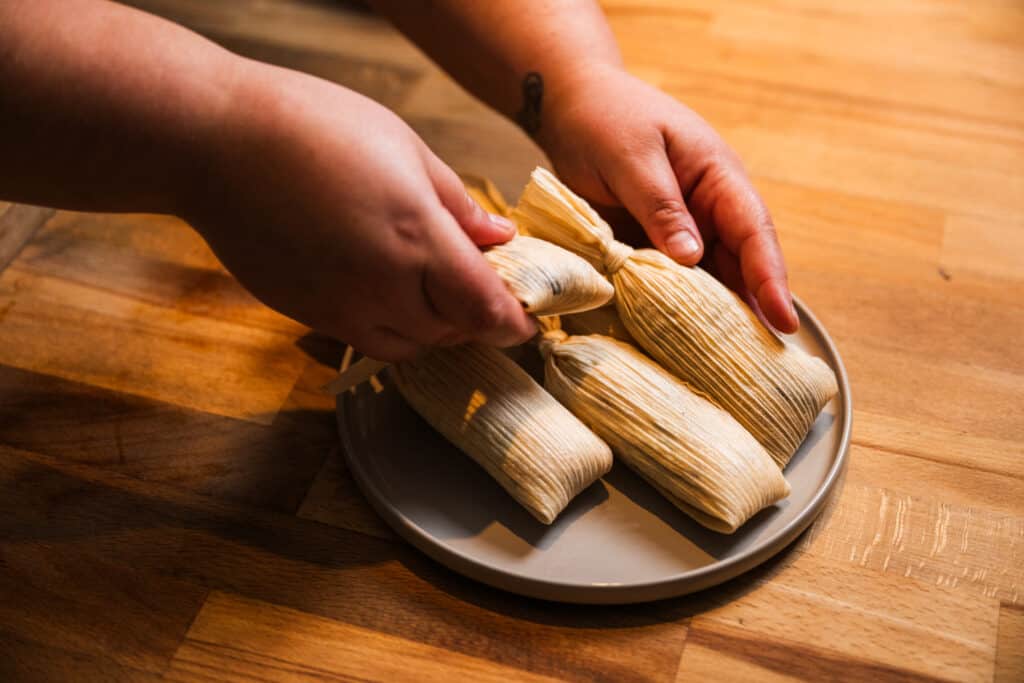 woman putting a sweeet tamale in a stack of tamales on a plate