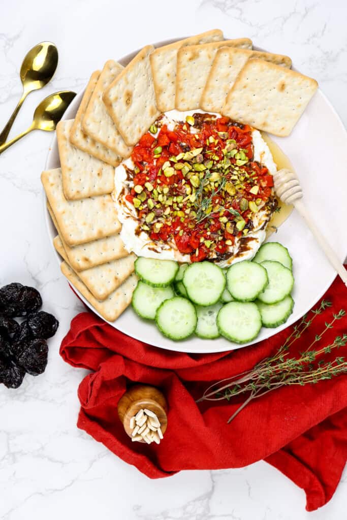 whipped feta dip on a platter with crackers, cucumbers and a red napkin