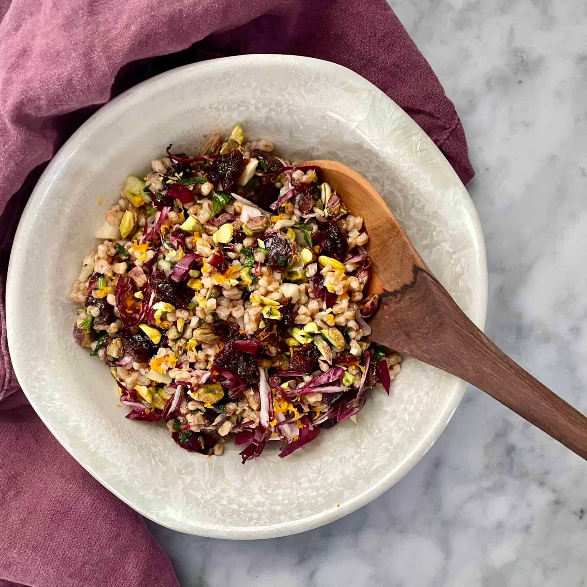 Bowl of Prune and Farro Salad Recipe with Zesty Herb Vinaigrette with wooden spoon