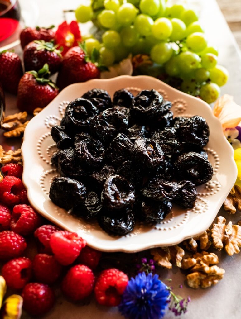 Bowl of prunes surrounded by grapes, strawberries, raspberries and walnuts