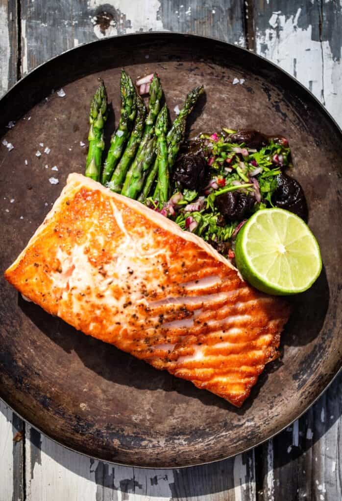 Roasted salmon plated with asparagus, salad greens and a halved lime
