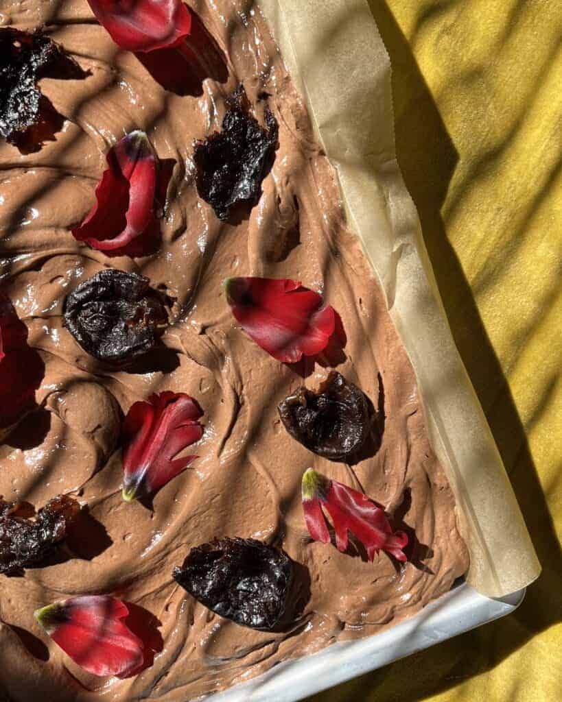 fudgy chocolate sheet cake in the pan topped with fresh flowers and prunes