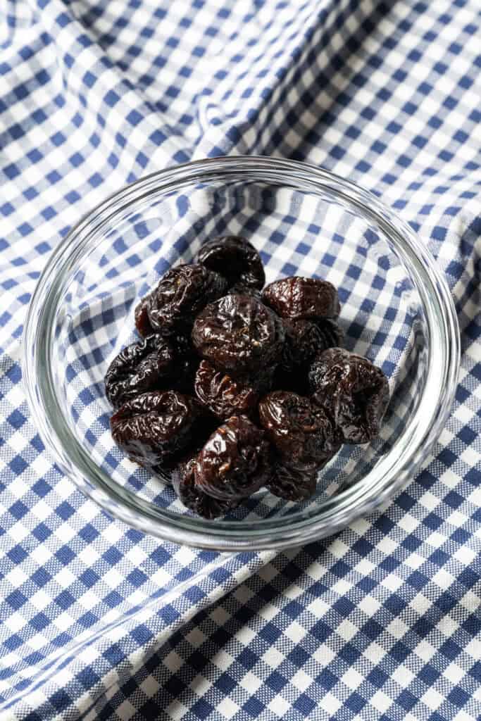 prunes in a glass bowl on a blue and white checkered cloth