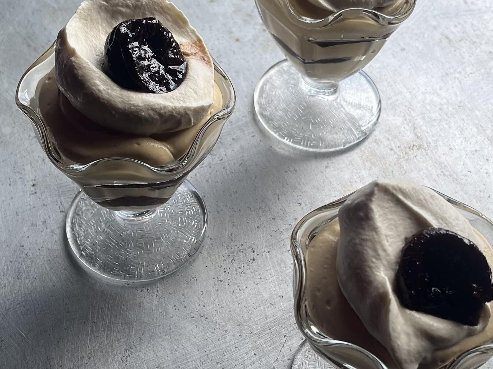 chicory creme diplomat in a parfait glass topped with whipped cream and a prune