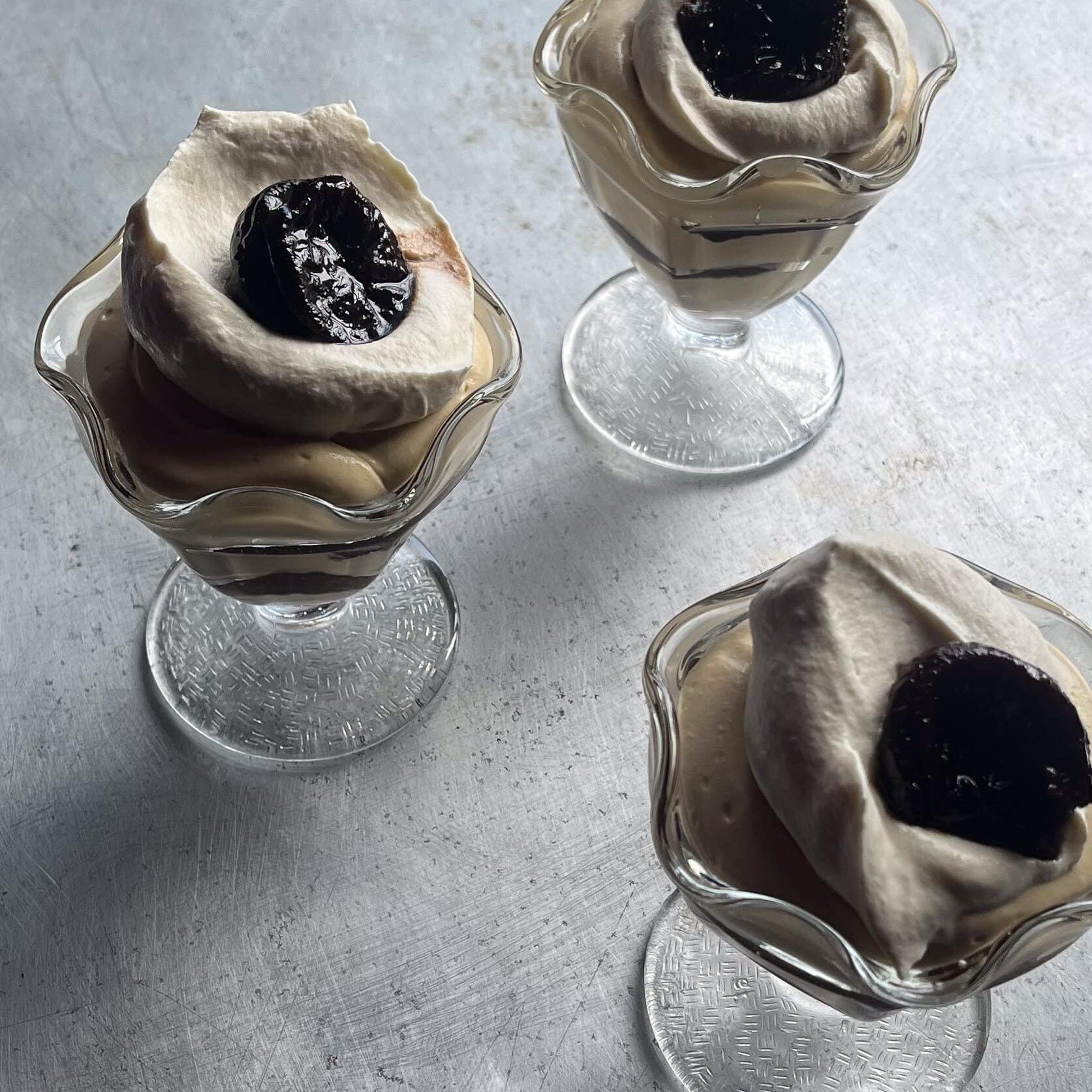 chicory creme diplomat in a parfait glass topped with whipped cream and a prune