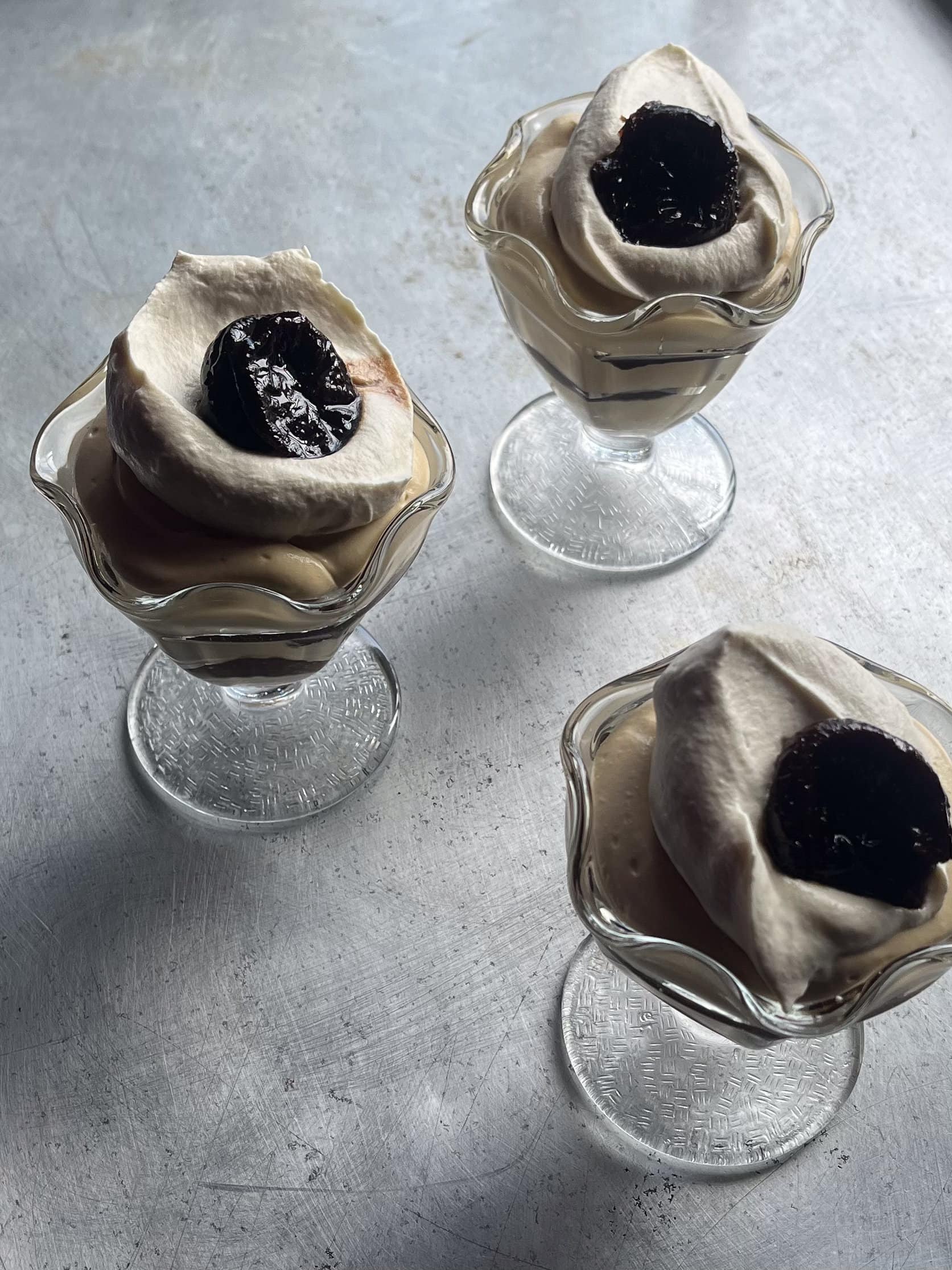 chicory creme diplomat in a parfait glass topped with whipped cream and a prune