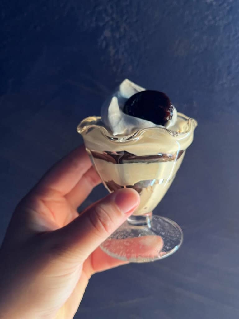 woman's hand holding a layered chicory diplomat cream layered with prune caramel in a parfait glass