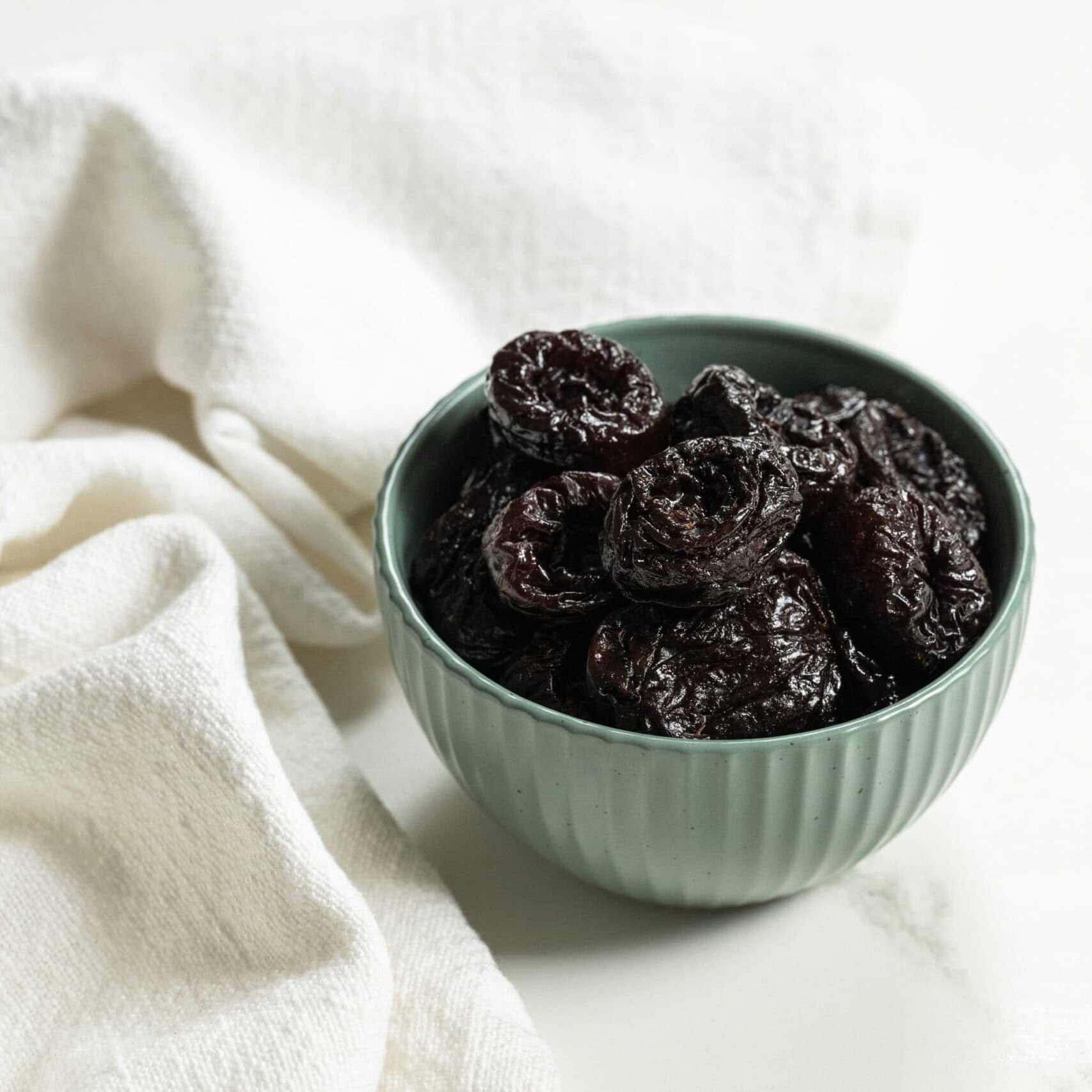 prunes in a blue bowl on a white table