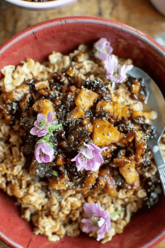 a bowl of oatmeal topped with chopped prunes, apples, nuts and flowers