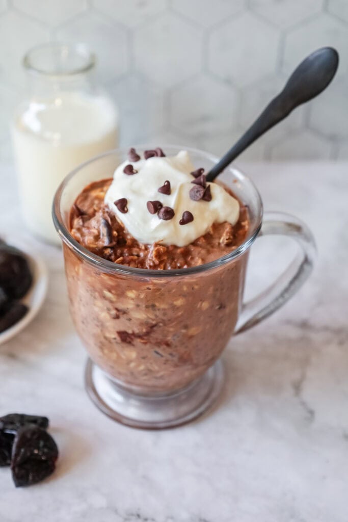 a glass mug with hot chocolate overnight oats topped with a dollop of yogurt and mini chocolate chips