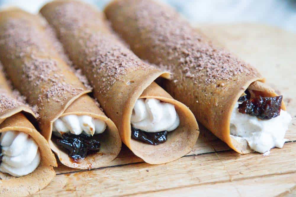 Four coffee soaked prune and whipped ricotta filled crepes on a serving board.