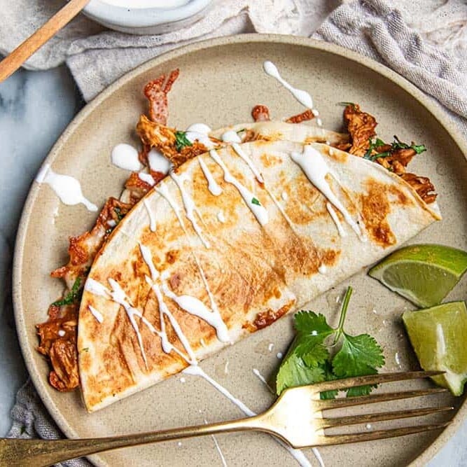 Chicken quesadilla with easy mole sauce served on a plate with cilantro, lime, and a drizzle of crema.