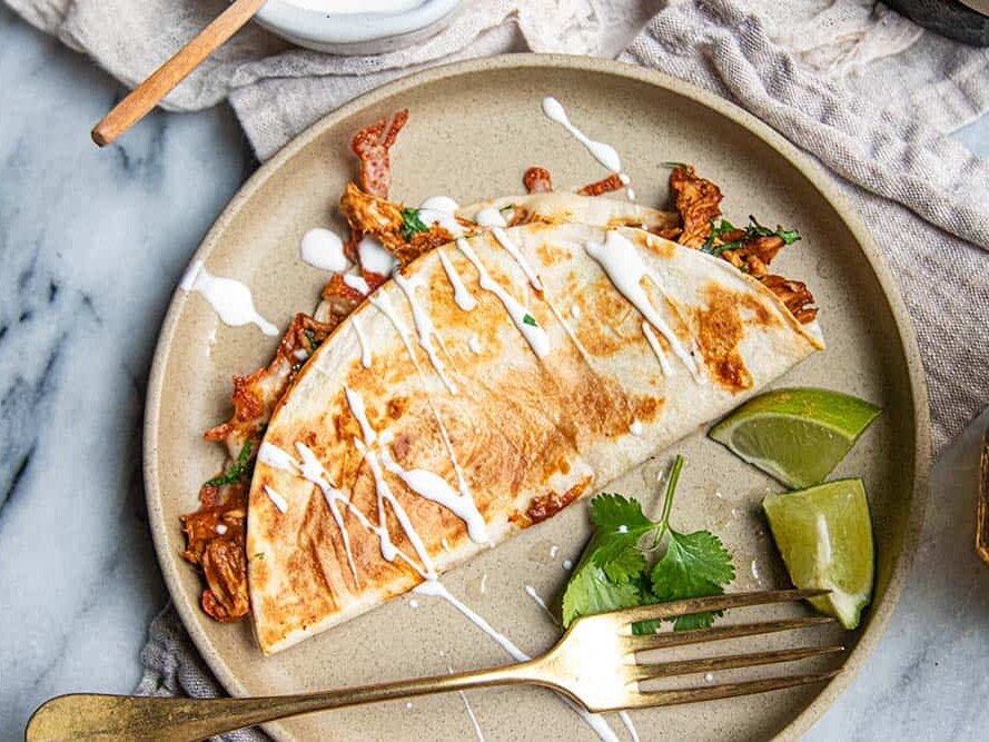 Chicken quesadilla with easy mole sauce served on a plate with cilantro, lime, and a drizzle of crema.