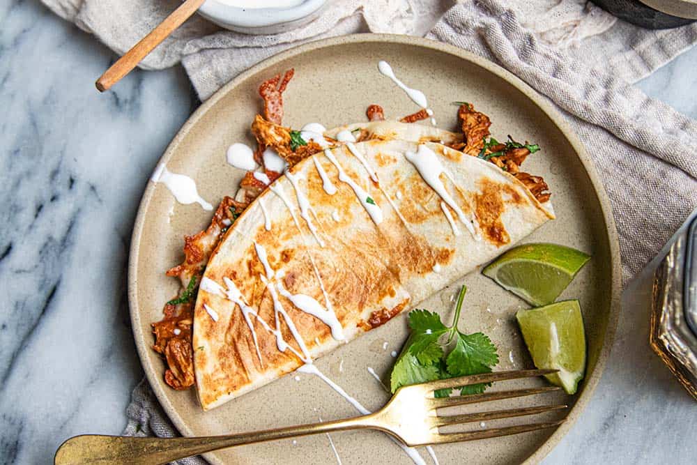 Chicken quesadilla with easy mole sauce served on a plate with cilantro, lime, and a drizzle of crema.