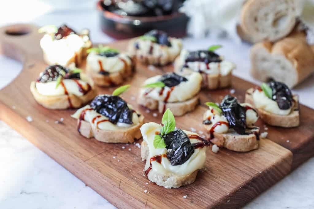 crostini topped with prunes and brie on a wooden board