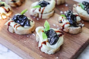 crostini topped with prunes and brie on a wooden board