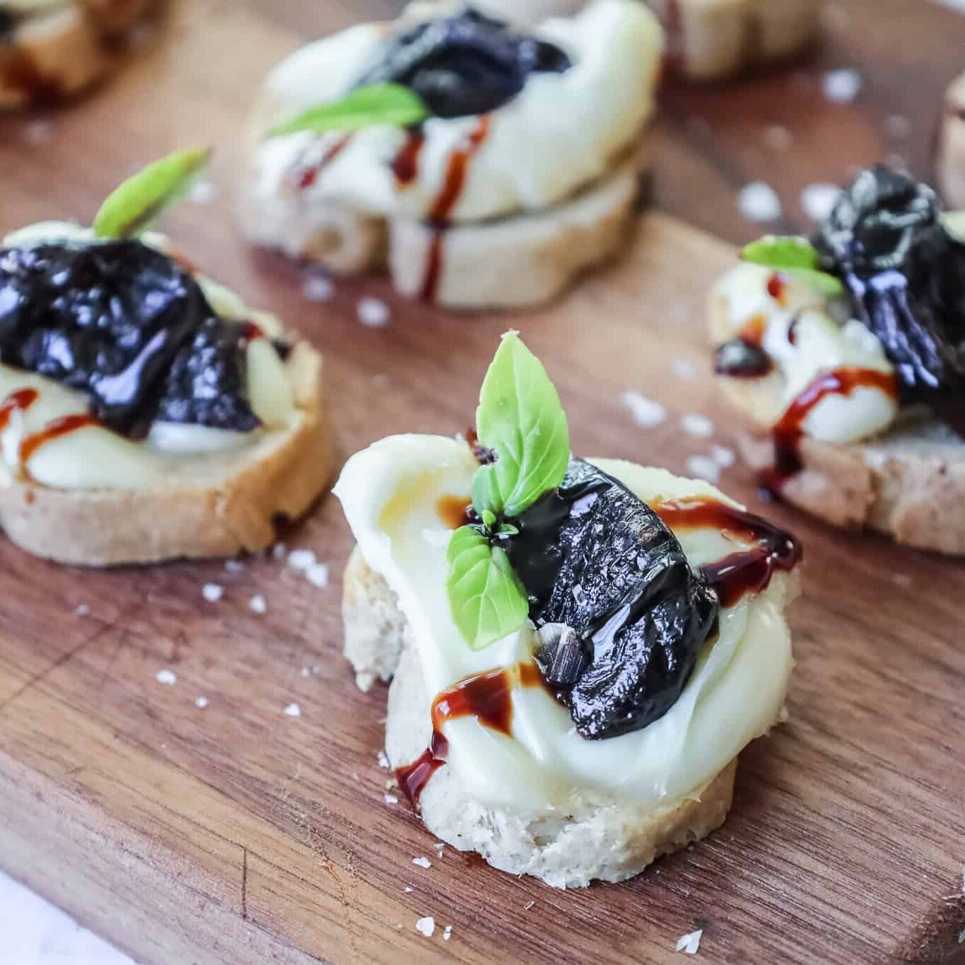 crostini topped with prunes and brie on a wooden board