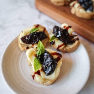 crostini topped with prunes and brie on a white plate