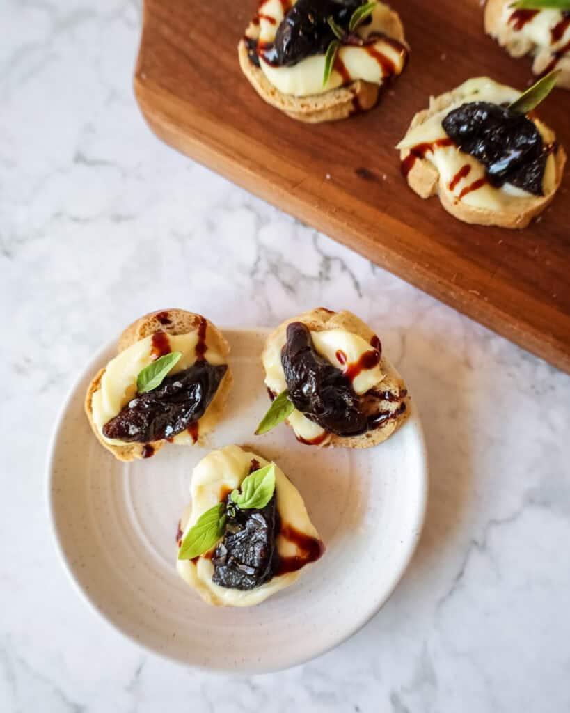 crostini topped with prunes and brie on a white plate