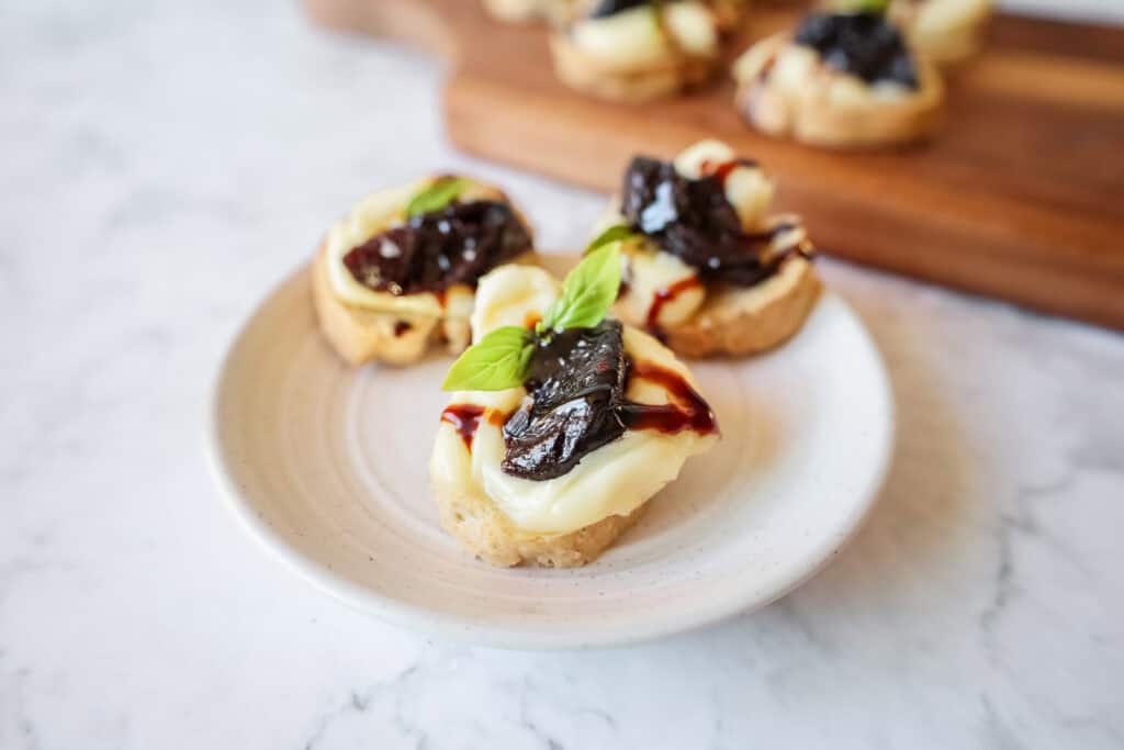 crostini topped with prunes and brie on a white plate