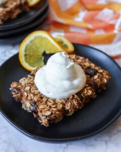 a slice of sheet pan baked oatmeal topped with yogurt and a sliced orange on a black plate