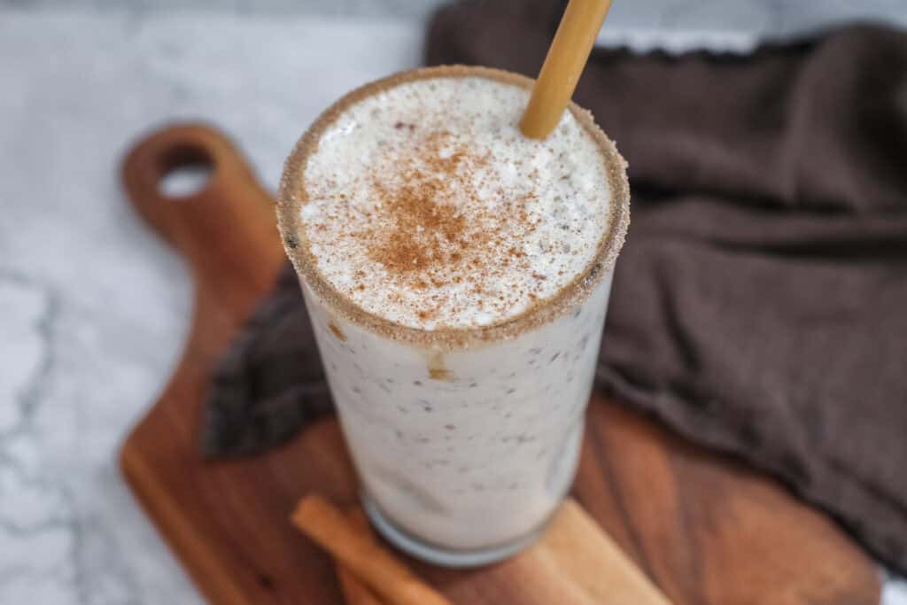 snickerdoodle smoothie in a glass with a bamboo straw on a wooden board