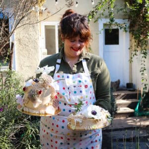 woman holding two prune coconut cake frosted with swiss buttercream and topped with fresh flowers