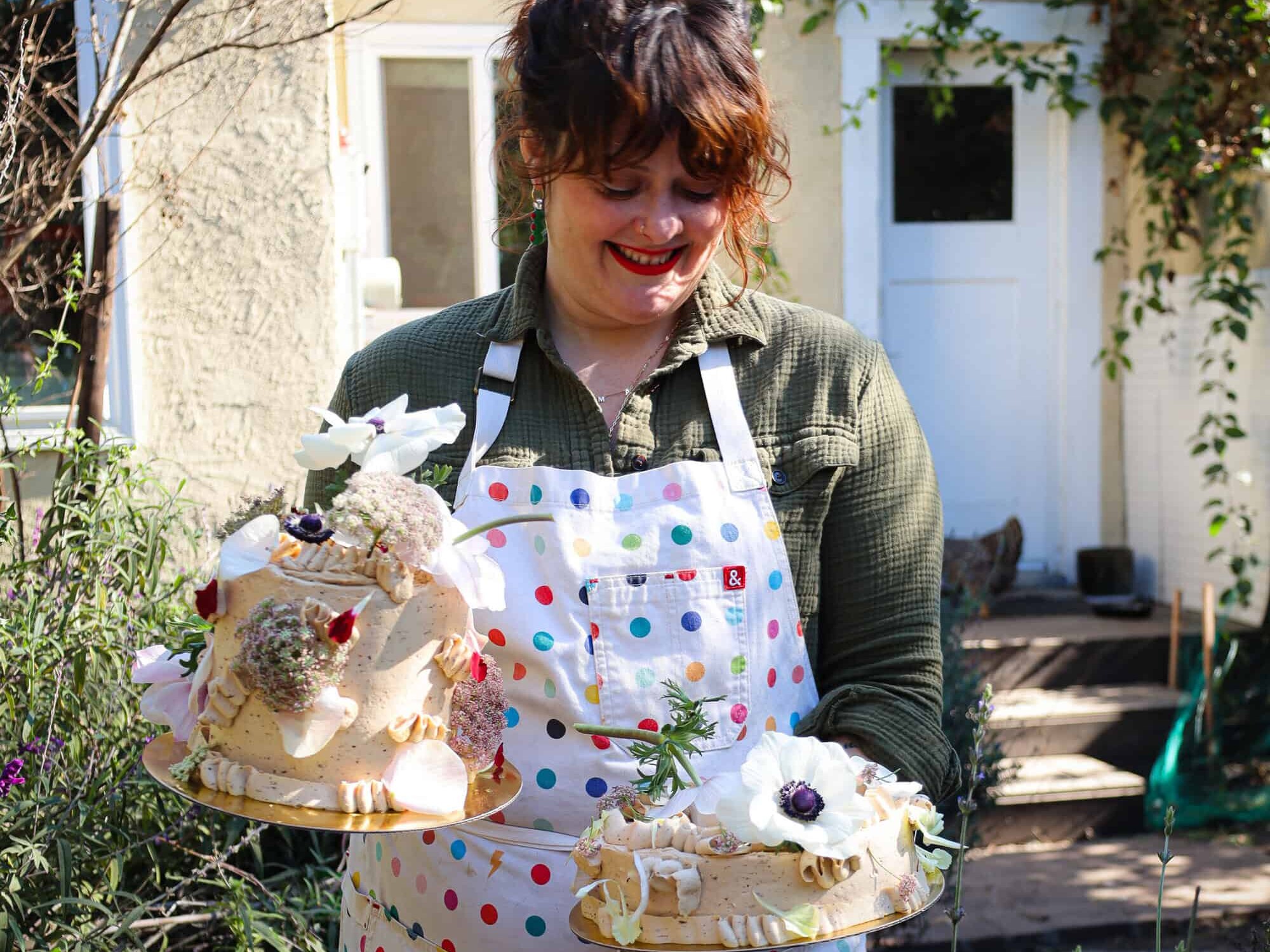 woman holding two prune coconut cake frosted with swiss buttercream and topped with fresh flowers