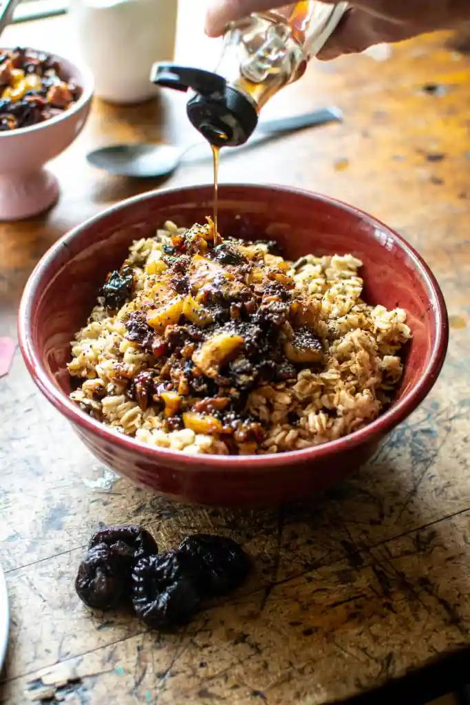 drizzling honey on a bowl of cinnamon apple oatmeal with prunes