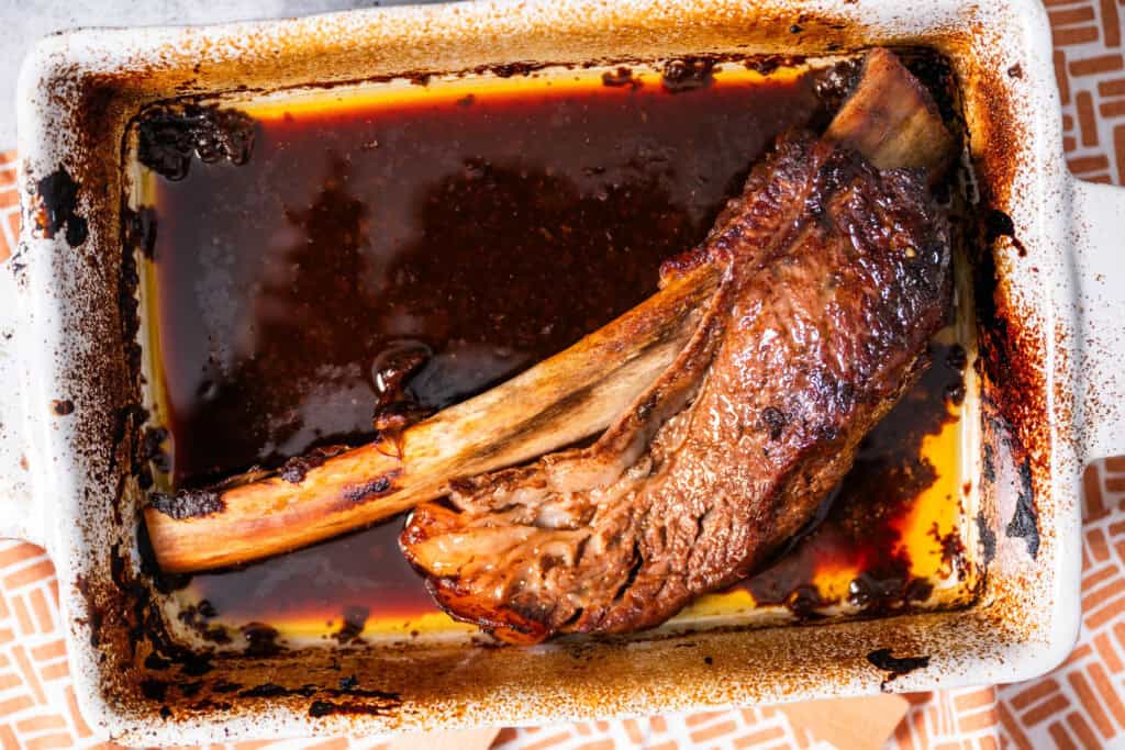 beef rib soaking in bbq sauce ina shallow bowl