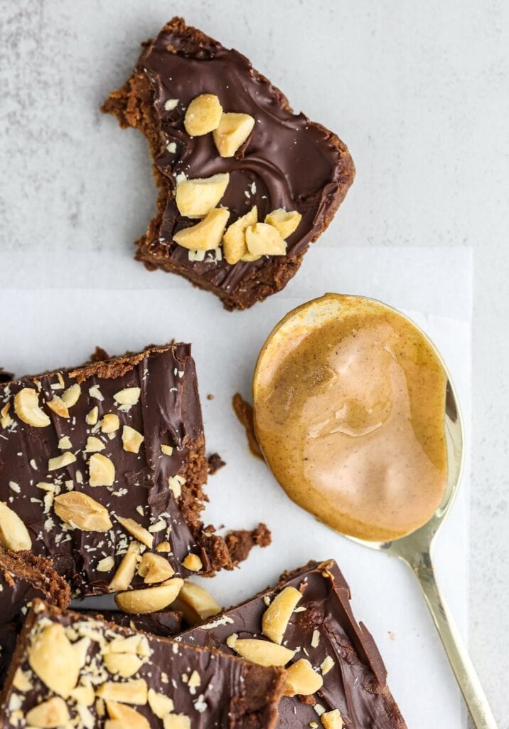 squares of nut topped peanut butter protein squares alongside a spoon of peanut butter