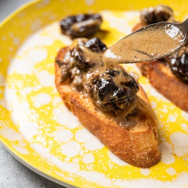spooning sauce over chicken livers with prunes on toast