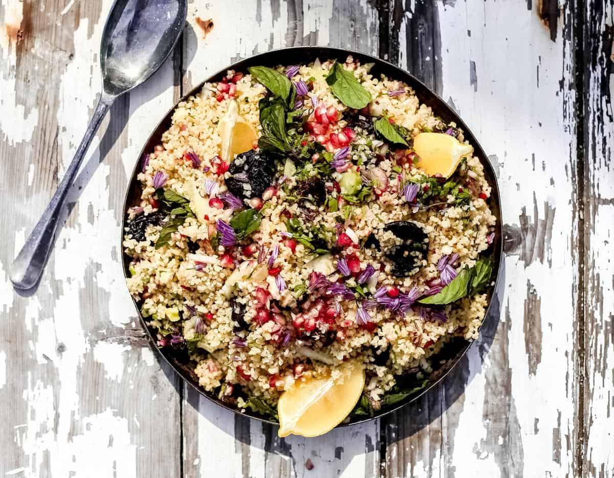 couscous salad with pomegranates in a black bowl on a wooden background