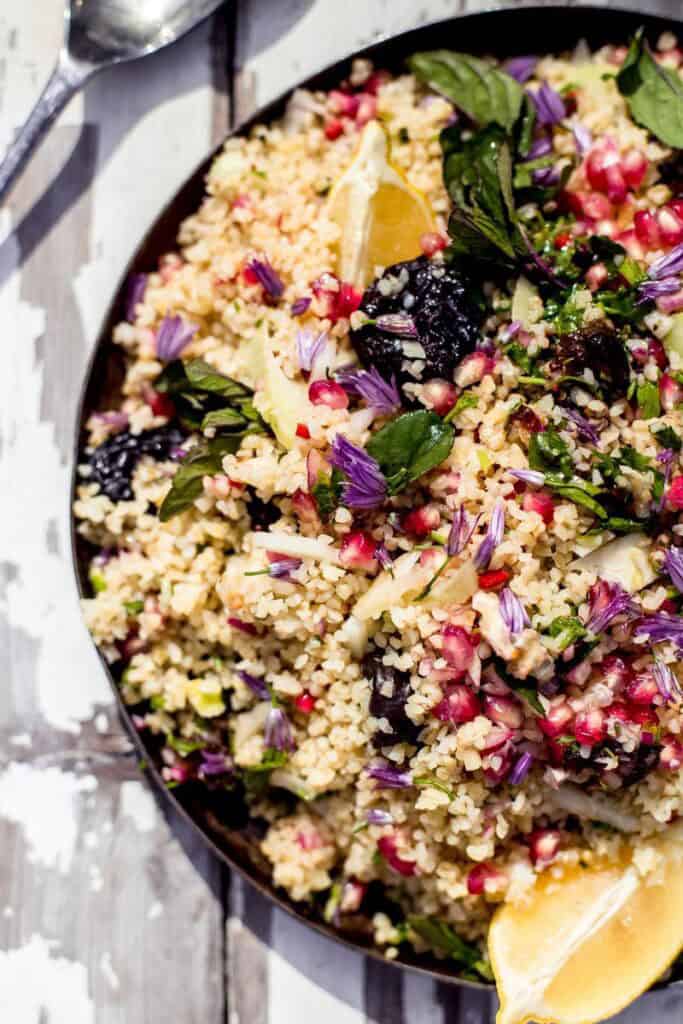 couscous salad with pomegranates in a black bowl on a wooden background